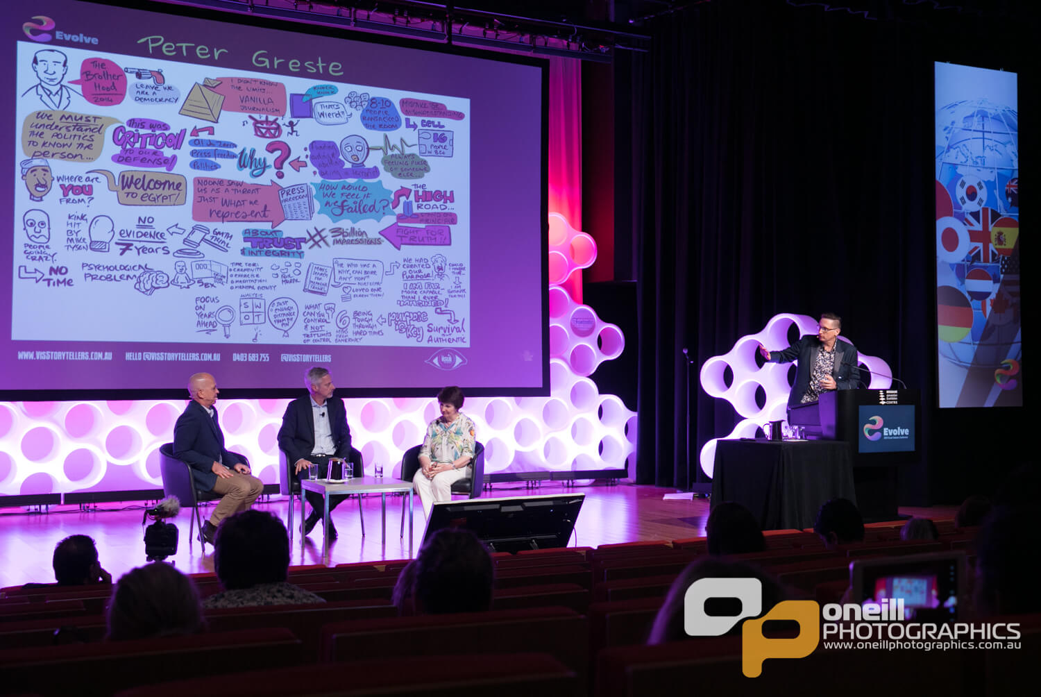 Conference panel discussion featuring Peter Greste, with a whiteboard illustration displaying key concepts and quotes related to storytelling and communication; engaging audience in a visually dynamic setting.