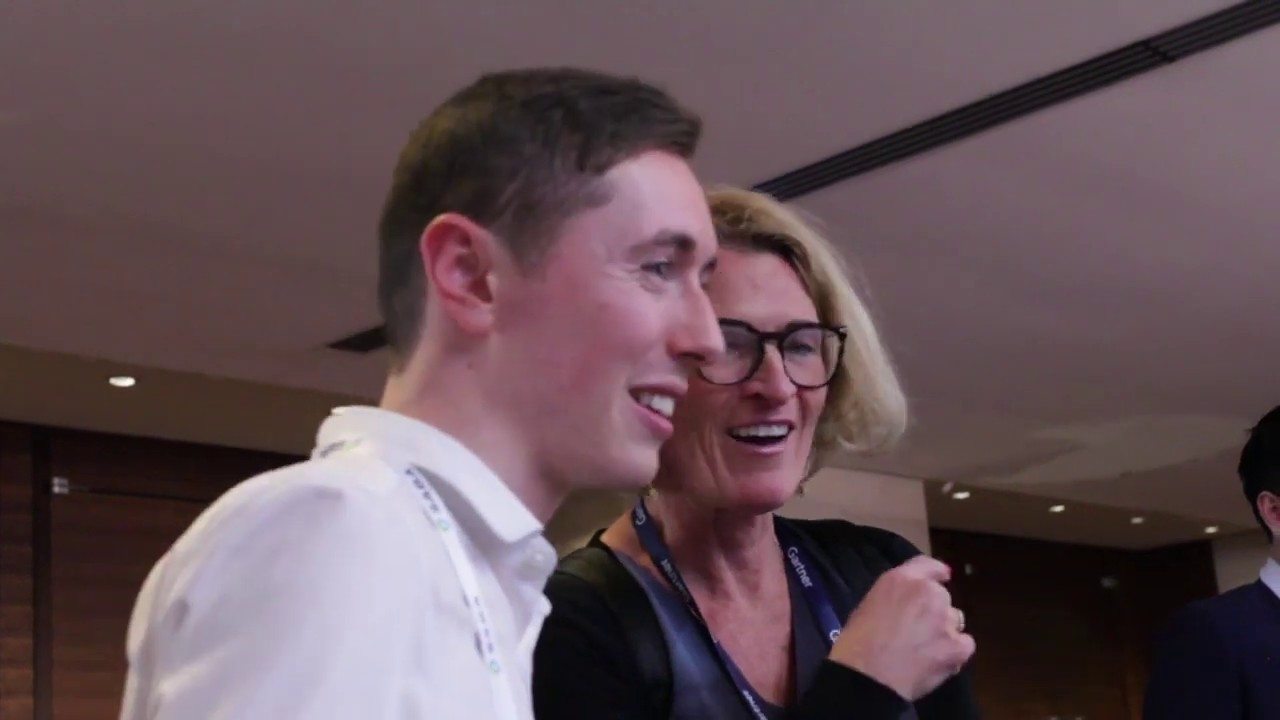 Two smiling individuals engaged in conversation at a networking event, surrounded by a professional setting, reflecting the interactive atmosphere of the Visual Storytellers Group's engagement efforts at conferences.