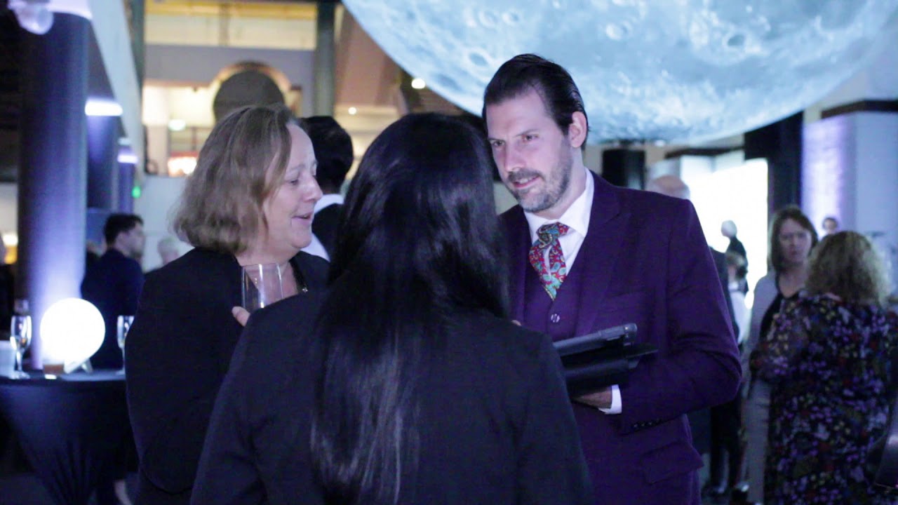 Group of professionals engaging in conversation at an event, with a large illuminated moon backdrop, highlighting networking and collaboration in a creative atmosphere.