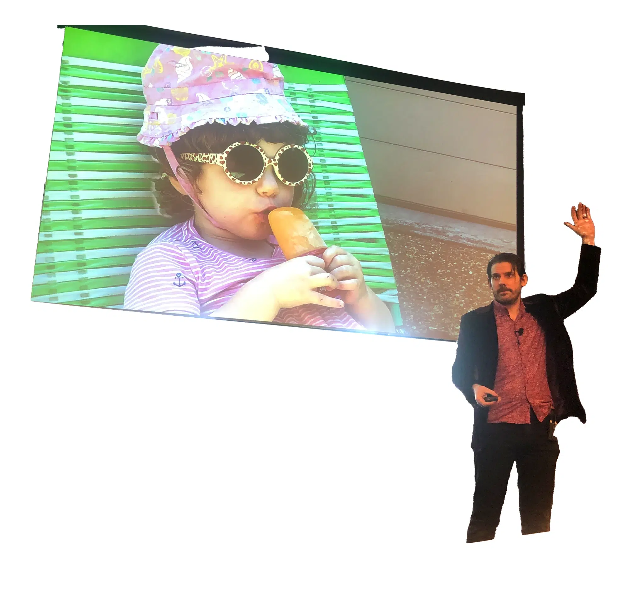 A man giving a presentation stands next to a large projected image of a young child